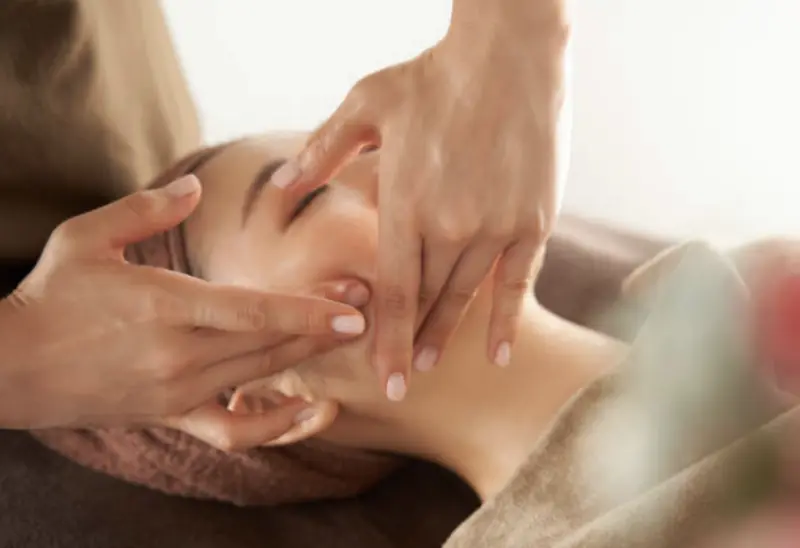 Mains de praticienne massant le visage d’une cliente
