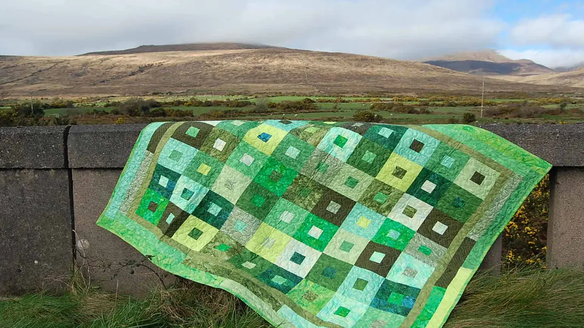 Green patchwork quilt draped over a stone wall